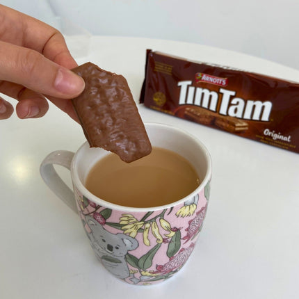 A partially bitten chocolate Tim Tam being dipped into a hot tea, enjoying the Tim Tam Slam